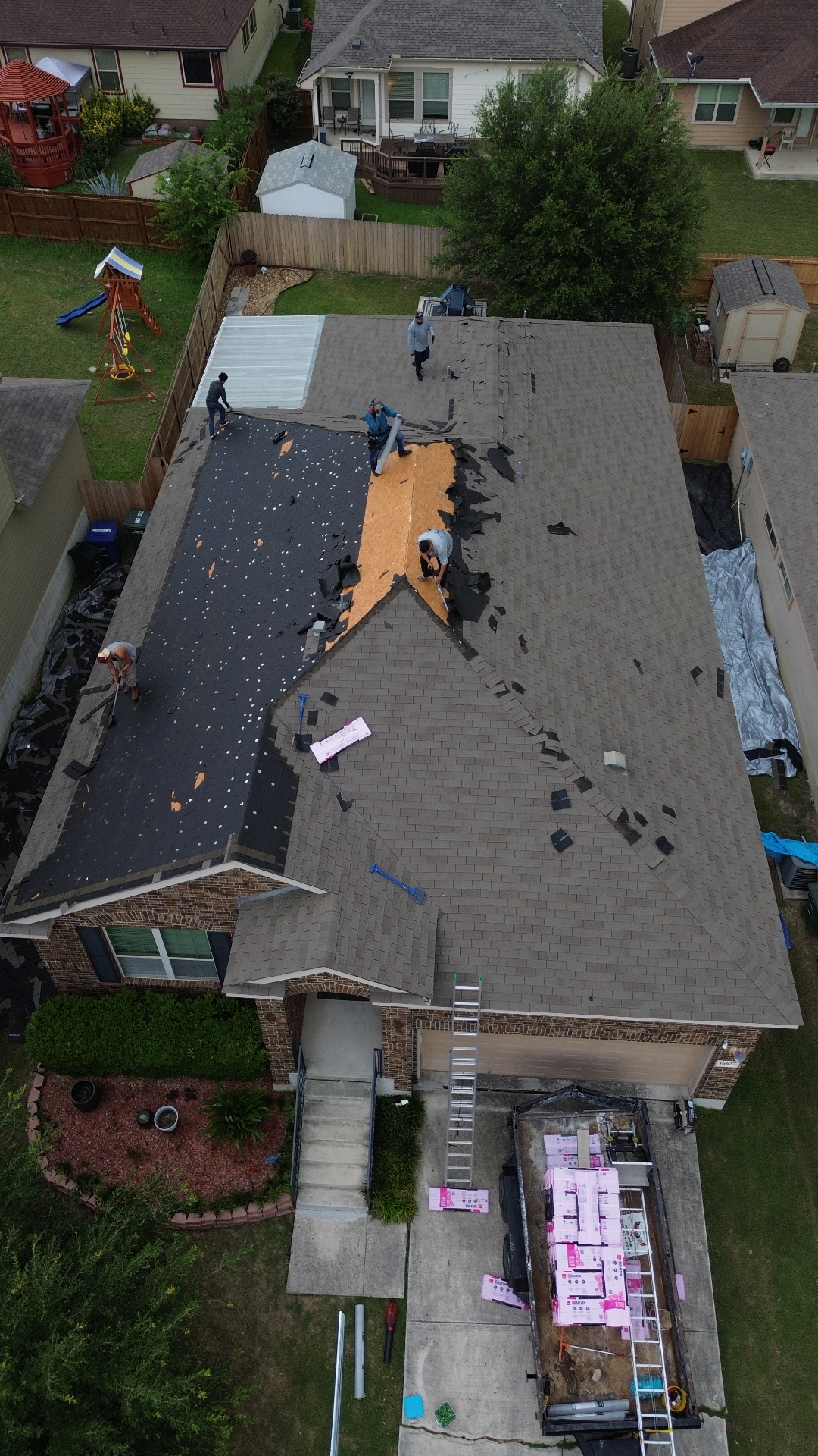 Aerial before photo of a San Antonio, TX home mid roof replacement with old shingles torn off, exposed decking, and crew working on the roof.