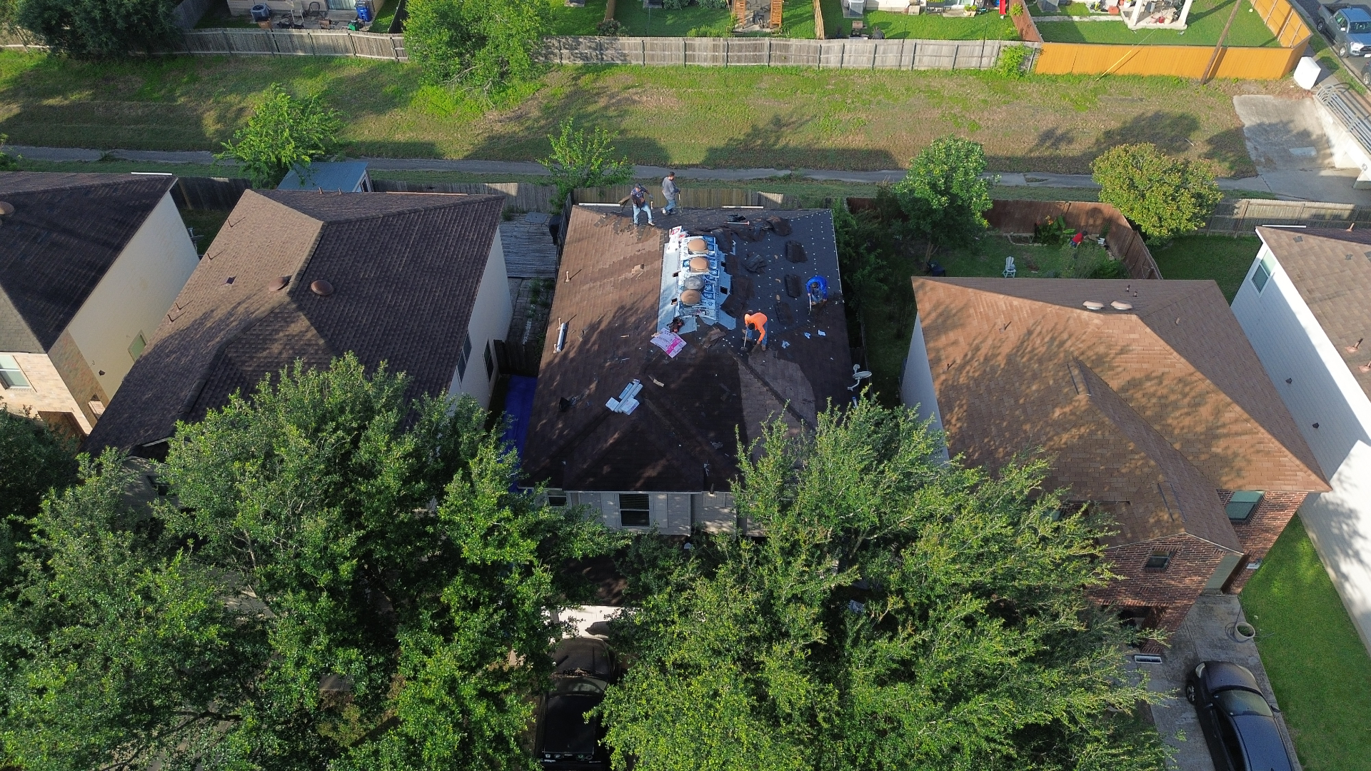 Aerial before photo of an Austin, TX home with crew tearing off the old roof, exposed decking, and underlayment in progress.