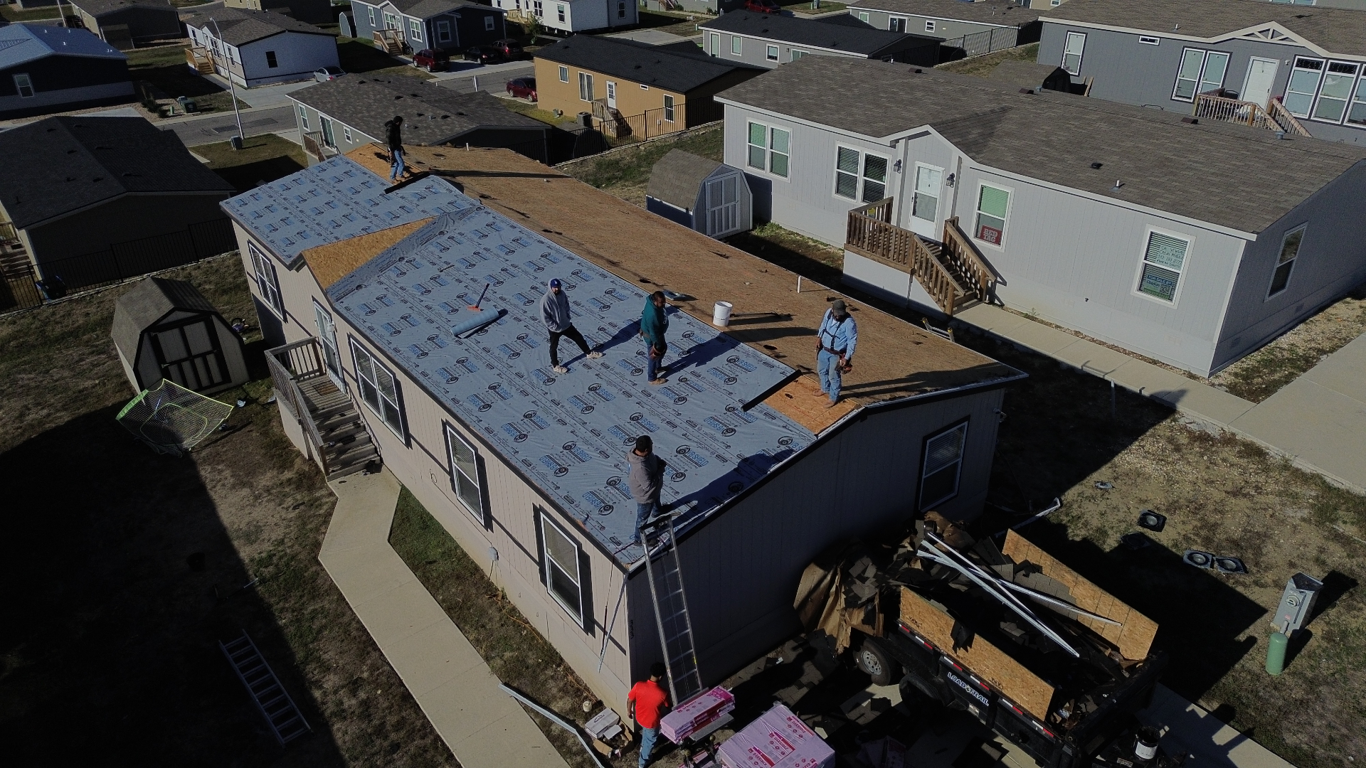 Aerial before photo of a Kyle, TX home mid roof replacement with synthetic underlayment installed and crew working on the deck.